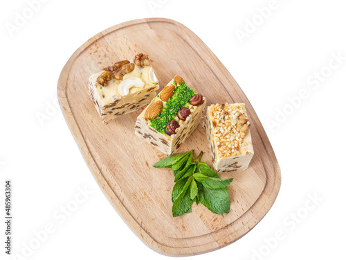 Three pieces of halva with raisins on a wooden board. Halva is decorated with walnuts, almonds, pistachios, fresh mint. White background, isolate. National sweets, organic desserts concept, top view