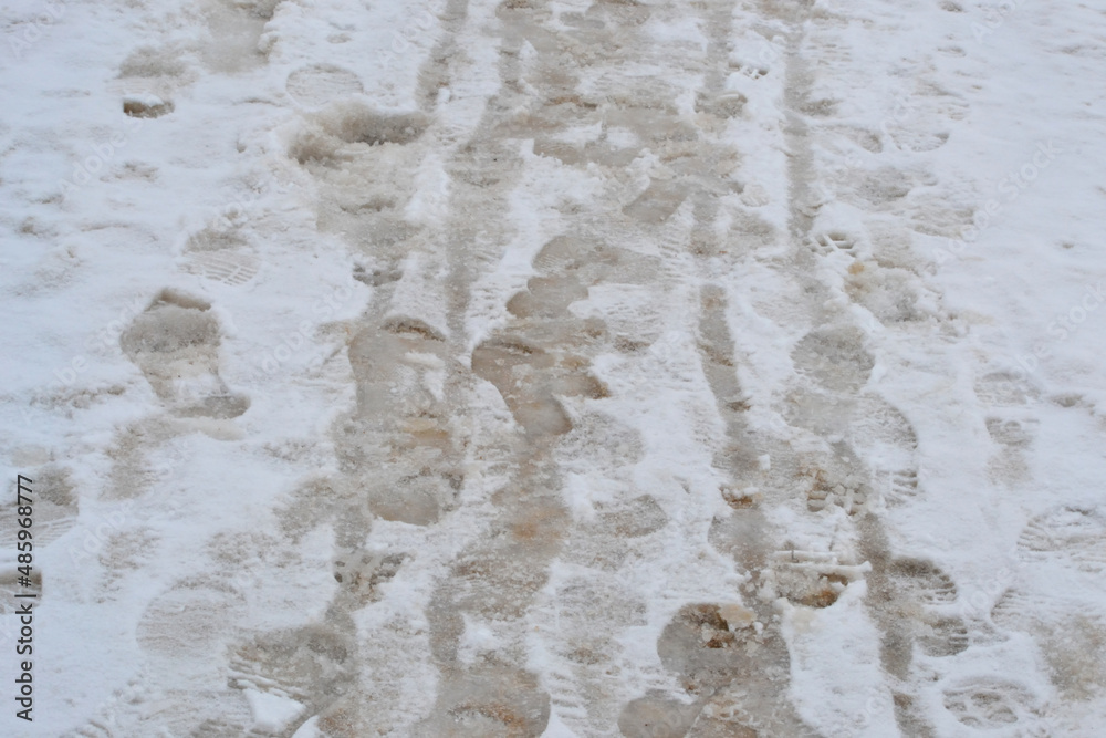 Fototapeta premium Footprints in slush on a city sidewalk after a snowstorm viewed at surface level