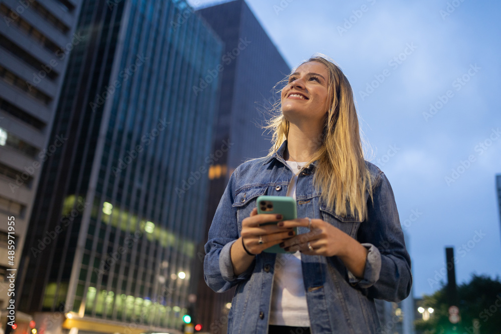 Young woman using a smartphone at night time with city view landscape in the background. High quality photo Young woman using a smartphone at night time with city view landscape in the background. High quality photo