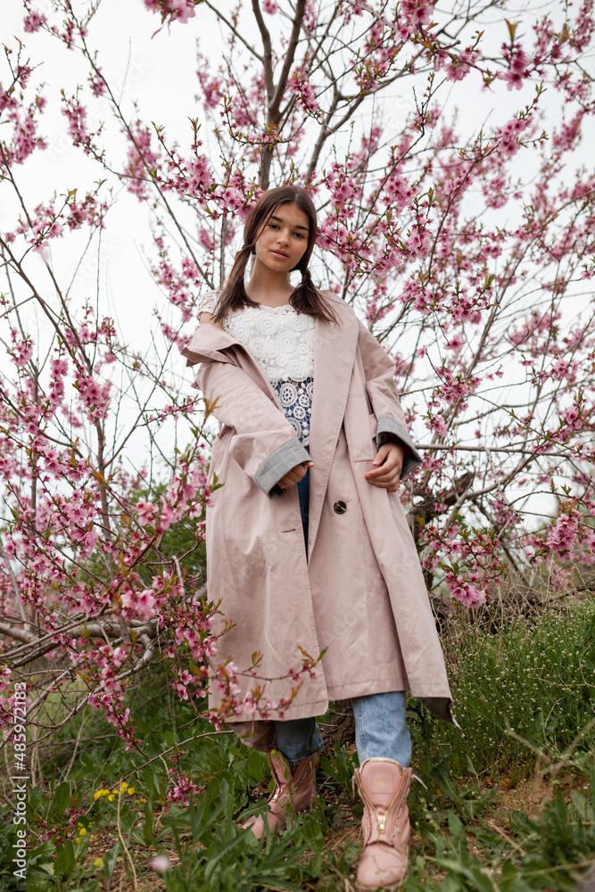 beautiful girl in spring peach garden. Teenager dressed in raincoat, jeans