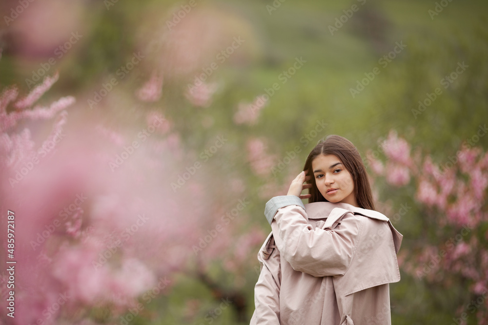 beautiful girl in spring peach garden. Teenager dressed in raincoat, jeans beautiful girl in spring peach garden. Teenager dressed in raincoat, jeans
