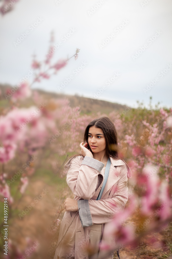 beautiful girl in spring peach garden. Teenager dressed in raincoat, jeans beautiful girl in spring peach garden. Teenager dressed in raincoat, jeans