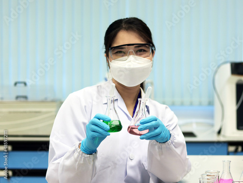 The scientist wear PPE and holds an Erlenmeyer flask laboratory, with green and pale pink solvent solution from reaction indicator acid titration experiment, analysis compounding in wastewater sample.