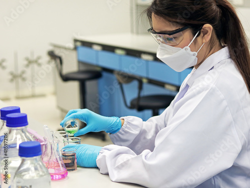 The scientist wears PPE do the chemical experiment in laboratory, with pale pink solvent solution from pouring reaction indicator acid titration experiment, analysis compounding in wastewater sample.