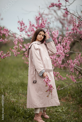 beautiful girl in spring peach garden. Teenager dressed in raincoat, jeans