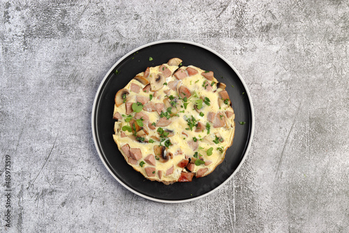 Omelet with sausage and mushrooms on a round plate on a dark gray background. Top view, flat lay