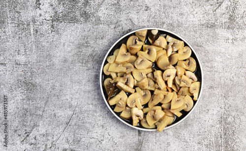 Pickled champignons mushrooms on a round plate on a dark gray background. Top view, flat lay