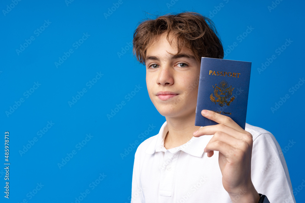 Portrait of glad handsome boy showing his passport going on vacation against blue background Portrait of glad handsome boy showing his passport going on vacation against blue background