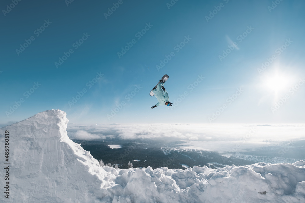 Snowboarder making high flip big air jump in clear blue sunny sky above mountains