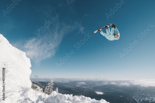 Snowboarder making high flip big air jump in clear blue sunny sky above mountains photo
