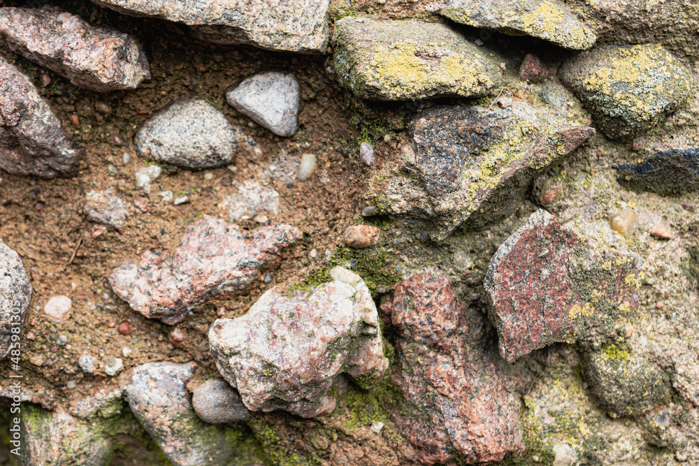 Textured old granite stone wall of large gray mossy stones as background.