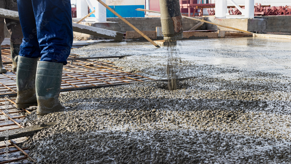 Builders workers pour concrete floor in industrial workshop. Legs in boots in concrete. Submission of concrete for pouring the floor. Monolithic concrete works. Builders workers pour concrete floor in industrial workshop. Legs in boots in concrete. Submission of concrete for pouring the floor. Monolithic concrete works.