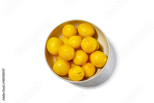 Lots of yellow plums in a white deep dish on a white background, view from above