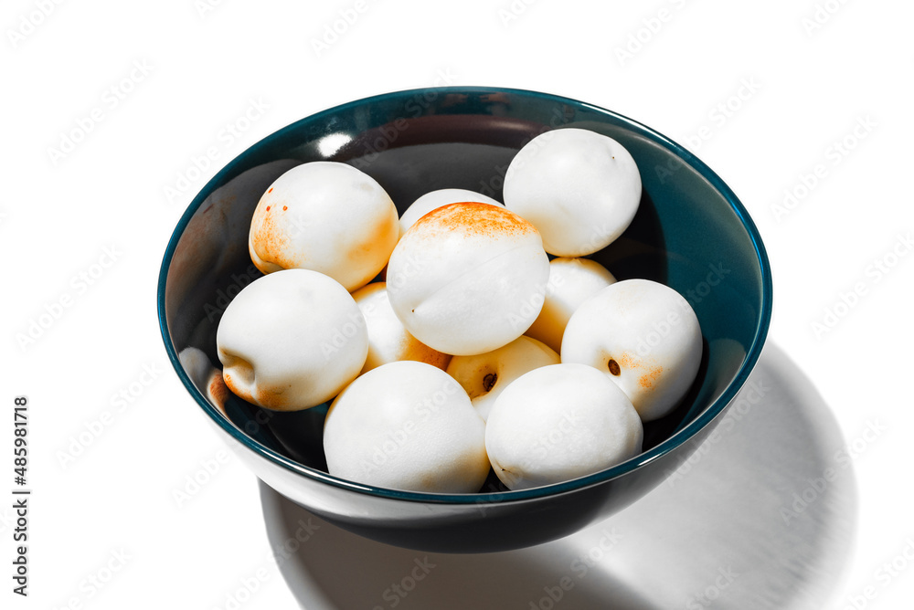 Unrealistic white and red apricots with a paper texture in a blue plate on a white background