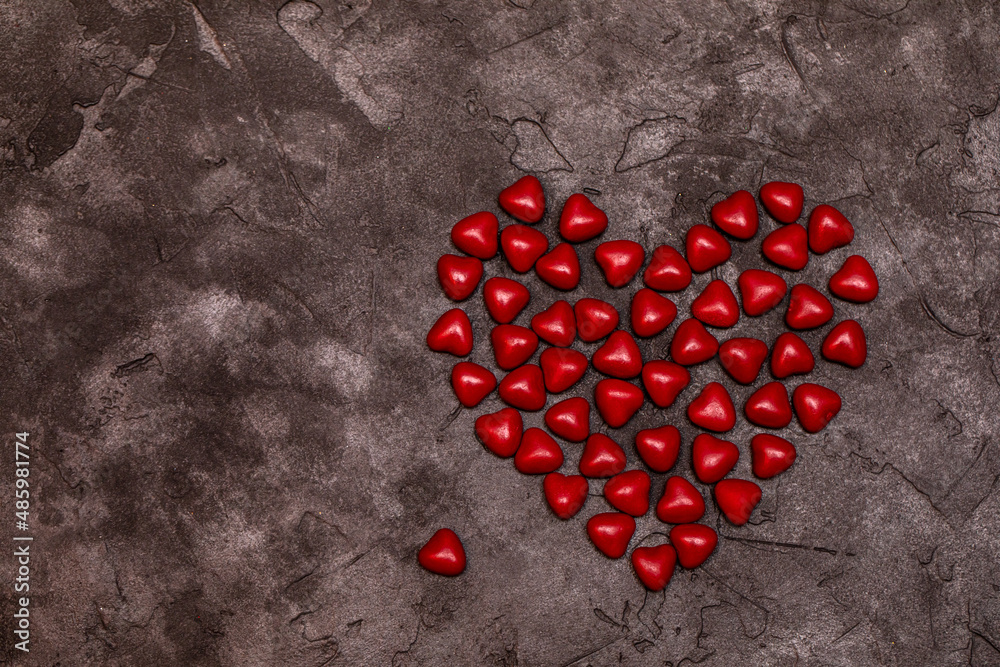 Symbol of love for February 14th. Red candy dragees are laid out in the shape of a heart on a dark background. Valentine's day concept. Symbol of love for February 14th. Red candy dragees are laid out in the shape of a heart on a dark background. Valentine's day concept.