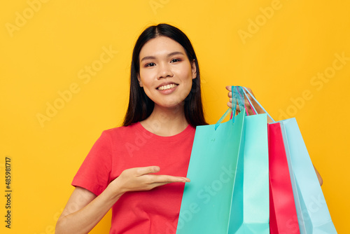 Portrait Asian beautiful young woman with multicolored shopping bags yellow background unaltered