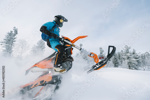 Jumping Snowbike rider in mountain valley in beautiful snow powder. Modify motorcycle with single ski in the front and special snowmobile-style track in the back instead of wheels