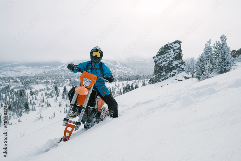 Snowbike rider in mountain valley in beautiful snow powder. Modify dirt bike with snow splashes and trail. Snowmobile sport riding, winter sunny day Snowbike rider in mountain valley in beautiful snow powder. Modify dirt bike with snow splashes and trail. Snowmobile sport riding, winter sunny day