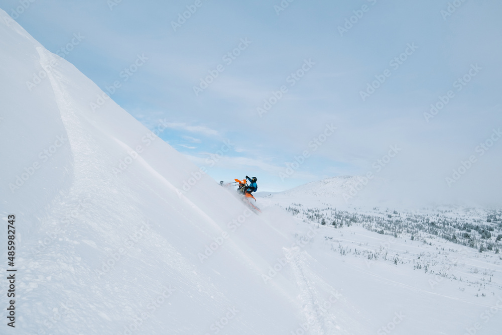Snowbike rider in mountain valley in beautiful snow powder. Modify dirt bike with snow splashes and trail. Snowmobile sport riding, winter sunny day Snowbike rider in mountain valley in beautiful snow powder. Modify dirt bike with snow splashes and trail. Snowmobile sport riding, winter sunny day