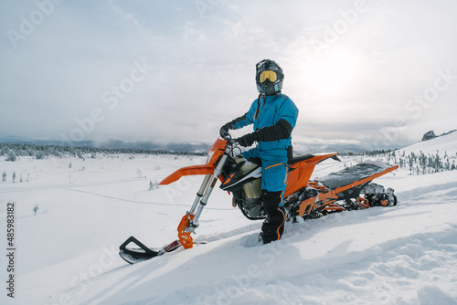 Snowbike rider in mountain valley in beautiful snow powder. Modify dirt bike with snow splashes and trail. Snowmobile sport riding, winter sunny day