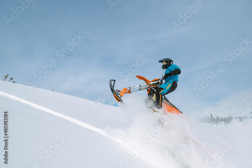 Snowbike rider in mountain valley in beautiful snow powder. Modify dirt bike with snow splashes and trail. Snowmobile sport riding, winter sunny day