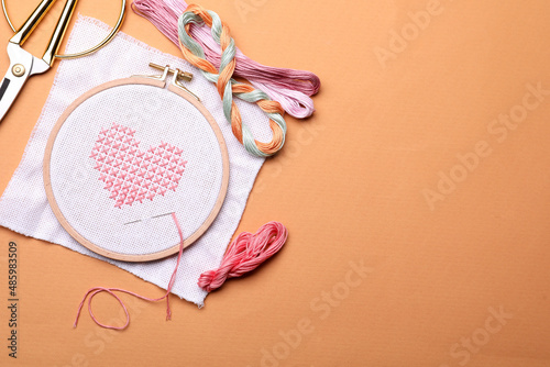 Flat lay composition with embroidery and different sewing accessories on orange background. Space for text photo