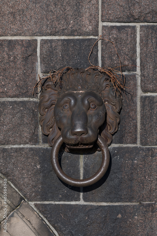Bronze lion head with a mouth ring at a stone wall a sunny winter day in Stockholm