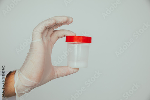 Doctor holding a plastic jar with sperm for semen analysis. Medical test in hospital