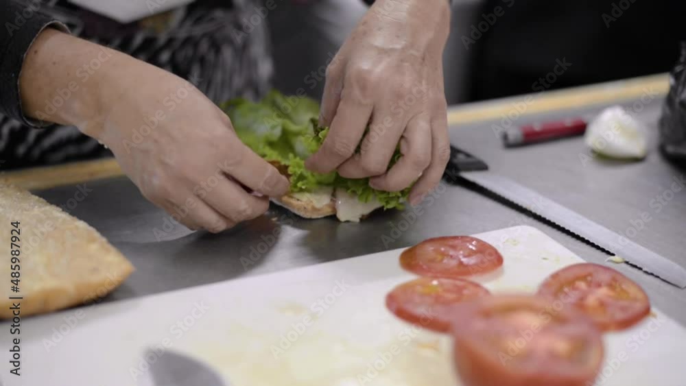 Woman chef cook preparing a salami ham pepperoni sandwich with lettuce and tomato on a baguette at a local cafe diner restaurant in Mexico Latin america. Healthy snack Woman chef cook preparing a salami ham pepperoni sandwich with lettuce and tomato on a baguette at a local cafe diner restaurant in Mexico Latin america. Healthy snack