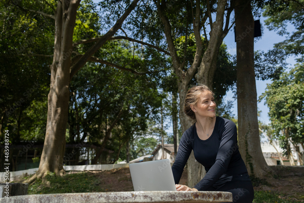 Young woman using a laptop at day time with a green park in the background. High quality photo Young woman using a laptop at day time with a green park in the background. High quality photo