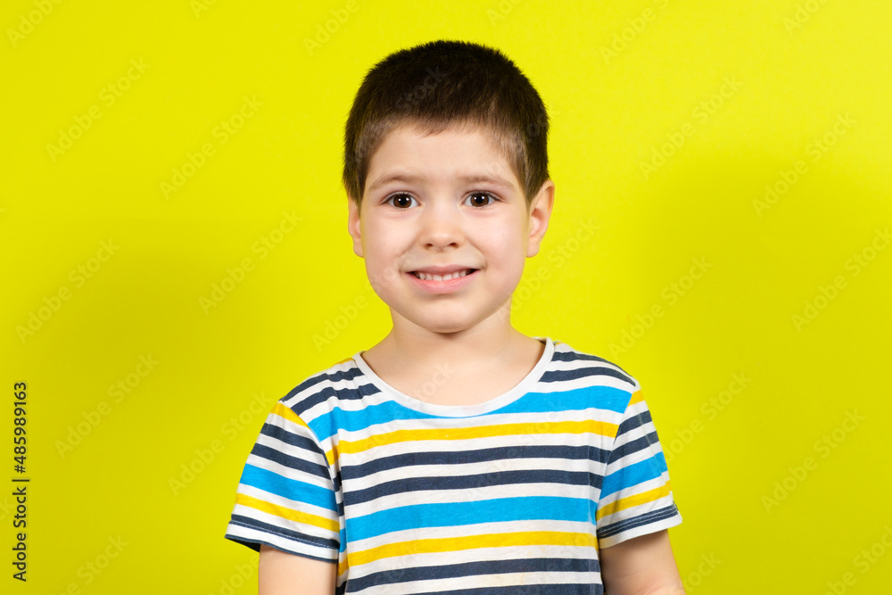 Portrait of a smiling handsome brunette boy of 4 years old in a striped blue T-shirt on a yellow background, copy the place for the text Portrait of a smiling handsome brunette boy of 4 years old in a striped blue T-shirt on a yellow background, copy the place for the text