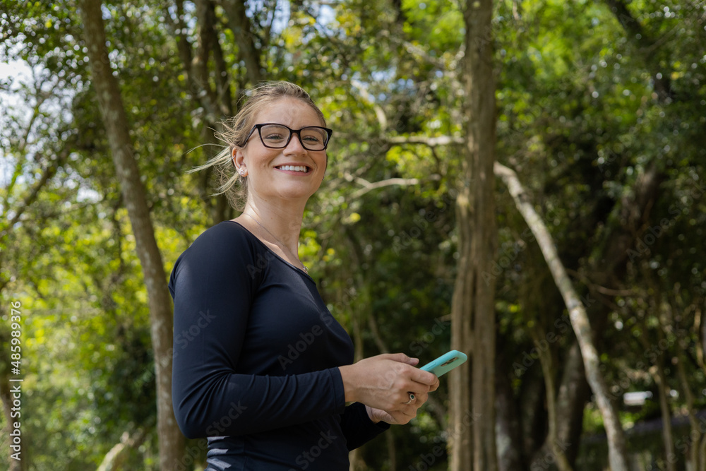 Young woman using a smartphone at day time with a green park in the background. High quality photo Young woman using a smartphone at day time with a green park in the background. High quality photo