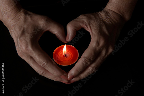 shapes heart with hands over burning candle on dark background