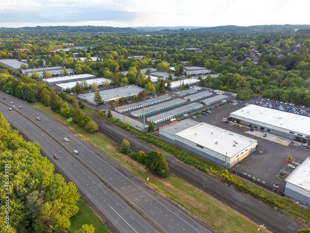 Shooting from a drone. Large highway, industrial buildings. Lots of greenery. In the background is a small green suburb with mountains in the distance. Real estate, travel, infrastructure.