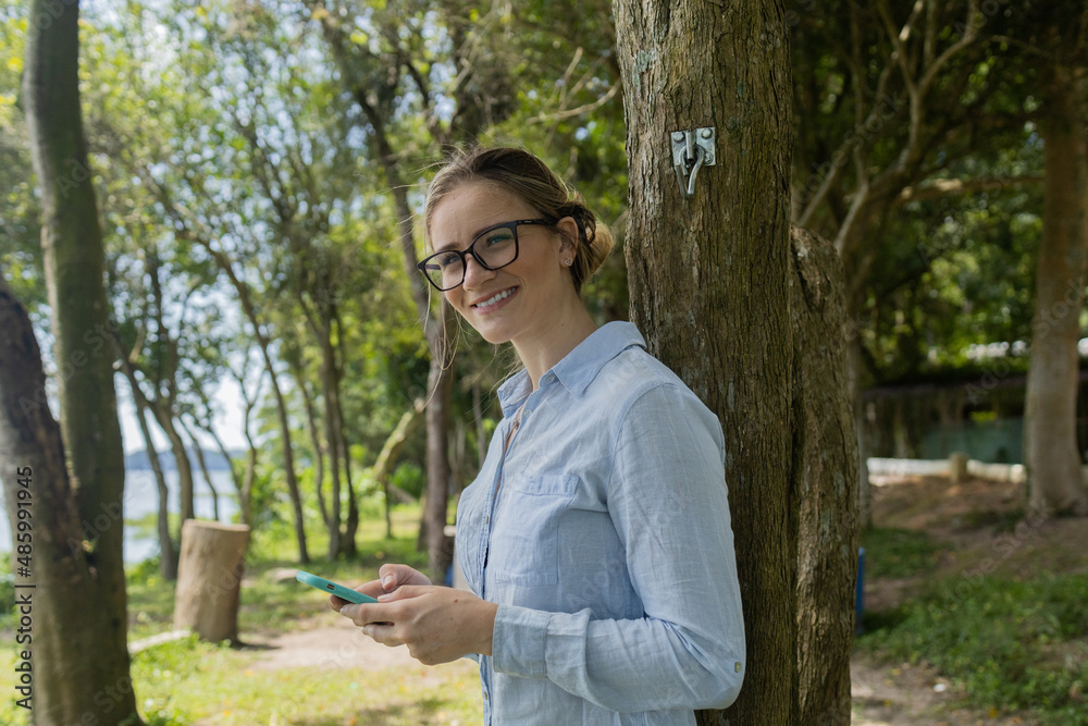 Young woman using a smartphone at day time with a green park in the background. High quality photo Young woman using a smartphone at day time with a green park in the background. High quality photo