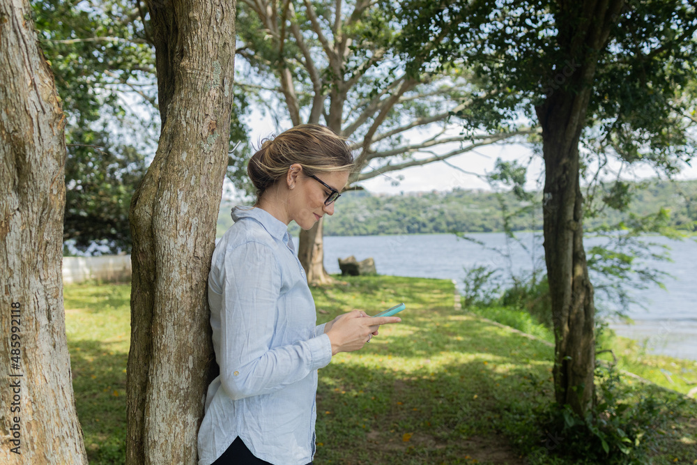 Young woman using a smartphone at day time with a green park in the background. High quality photo Young woman using a smartphone at day time with a green park in the background. High quality photo