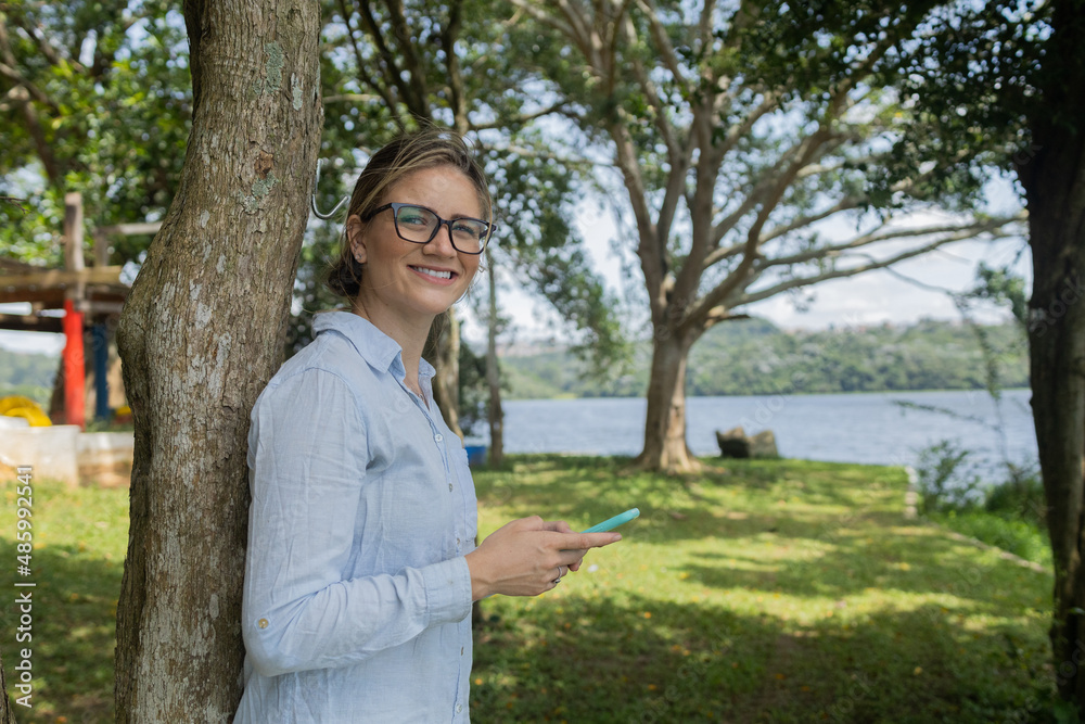 Young woman using a smartphone at day time with a green park in the background. High quality photo