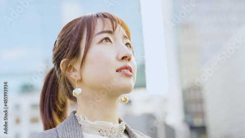 ビル街で空を見上げる若い女性
