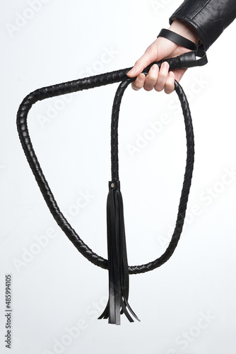 Close-up shot of a female hand in a leather sleeve holding a black leather whip with a fringe of leather straps and a loop for fixing on the wrist. The photo is made on the white background.