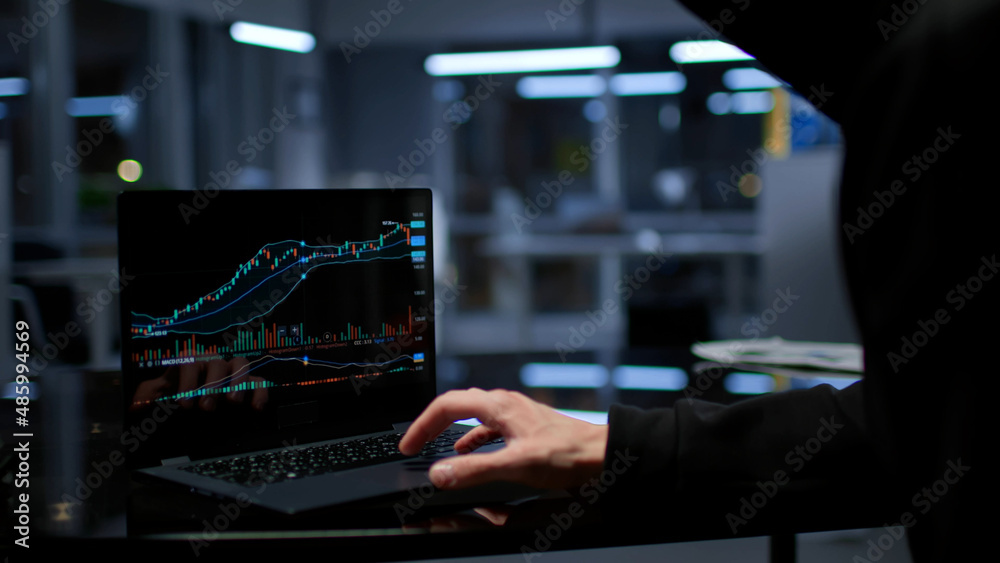 Young sly man trying to breach the system while giving bad commands on laptop in empty dark office Young sly man trying to breach the system while giving bad commands on laptop in empty dark office