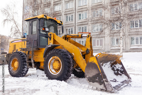 Big orange tractor cleans up snow from the road and loads it into the truck. Cleaning and cleaning of roads in the city from snow in winter. Snow removal after snowfall and blizzards.  © Анатолий Савицкий