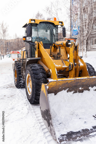 Big orange tractor cleans up snow from the road and loads it into the truck. Cleaning and cleaning of roads in the city from snow in winter. Snow removal after snowfall and blizzards.  © Анатолий Савицкий