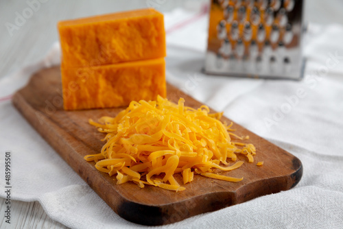 Shredded Sharp Cheddar Cheese on a rustic wooden board, side view. Close-up.