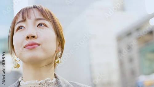 ビル街で空を見上げる若い女性