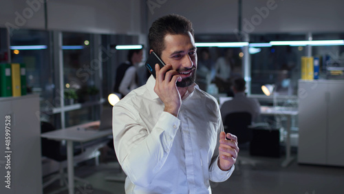 Excited businessman talking on smartphone and smiling standing in office