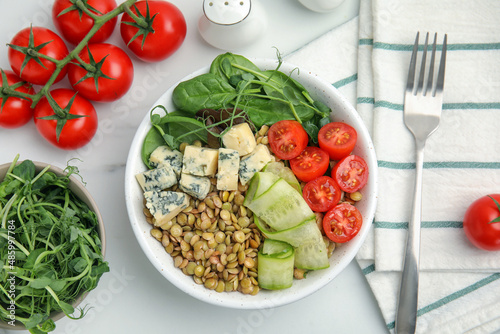 Delicious lentil bowl with blue cheese, tomatoes and cucumber on white marble table, flat lay