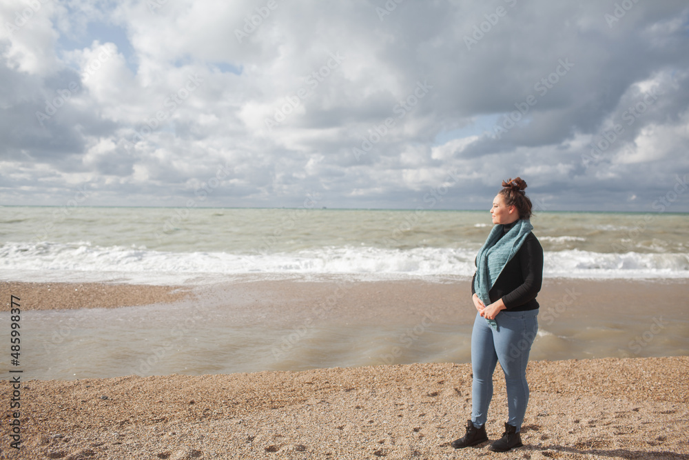 Beatuful woman with over weight body walking in the beach, The plus size model wearing jeans, the warm knitted blanket and sweater. the wind in the bich have fun with hairs Beatuful woman with over weight body walking in the beach, The plus size model wearing jeans, the warm knitted blanket and sweater. the wind in the bich have fun with hairs