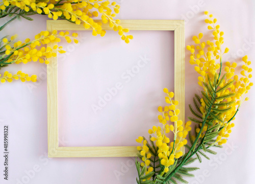 Top view of wooden empty frame with mimosa on a pink background. A beautiful composition of spring flowers with a place for a congratulatory text. Valentine's Day, Easter, Birthday, Happy Women's Day