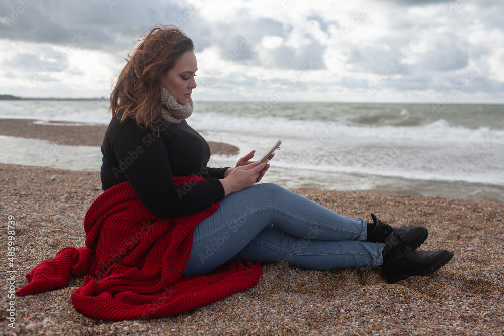 Beatuful woman with over weight body walking in the beach, The plus size model wearing jeans, the warm knitted blanket and sweater. the wind in the bich have fun with hairs