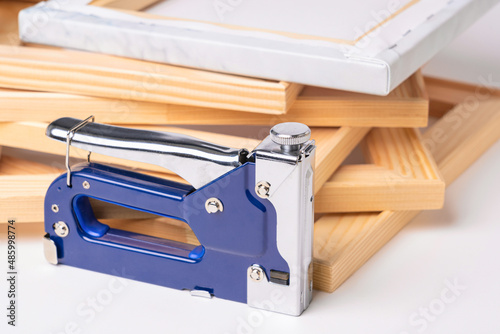 A stapler gun for canvas stretching, wooden frames and a finished canvas in the background. The production process of printed paintings and photographs on canvas photo